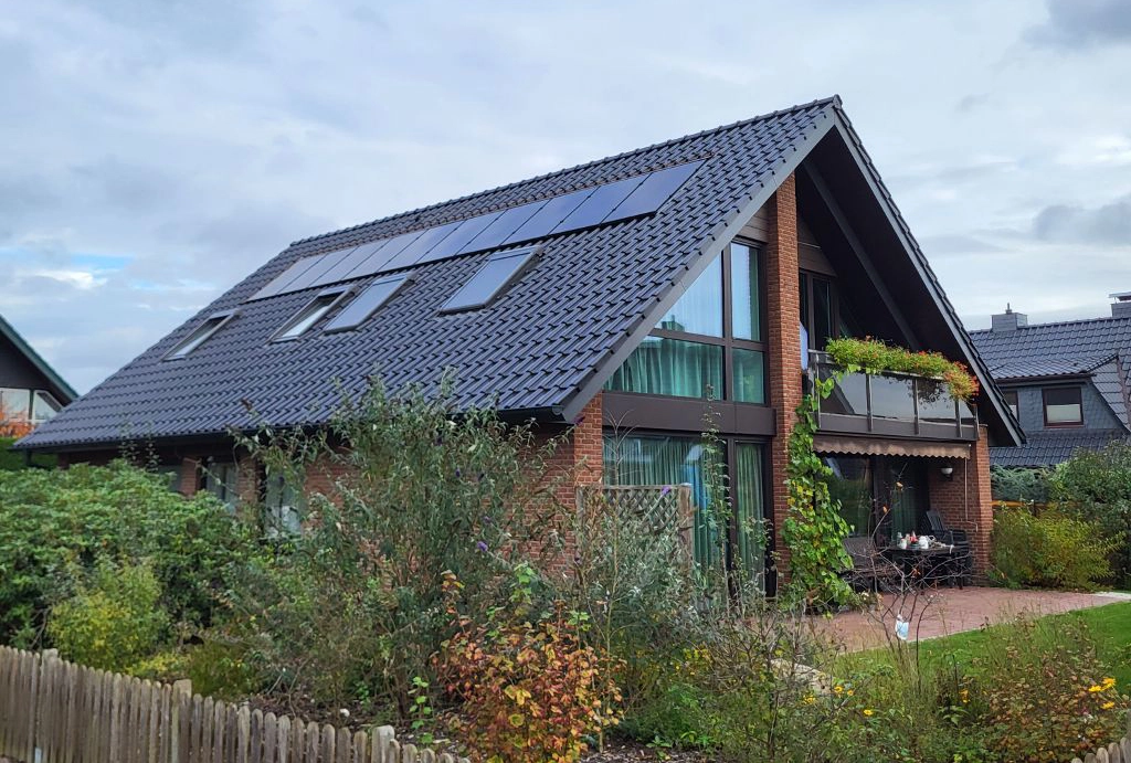 Modernes Einfamilienhaus mit dunklem Ziegeldach, integrierten Solarmodulen und Dachfenstern, umgeben von einem gepflegten Garten.