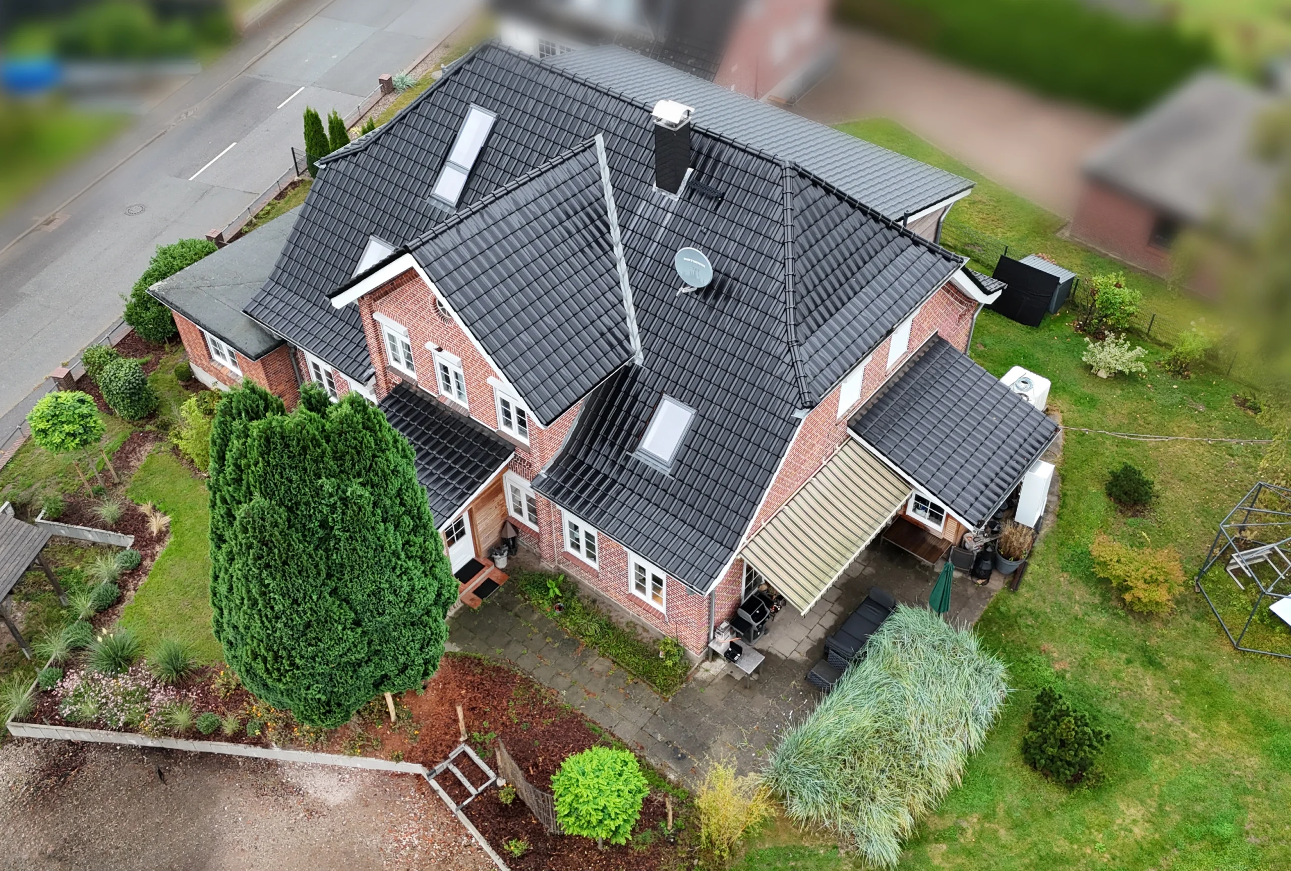 Luftaufnahme eines Einfamilienhauses mit neu gedecktem, dunklem Ziegeldach, Dachfenstern und gepflegtem Garten.