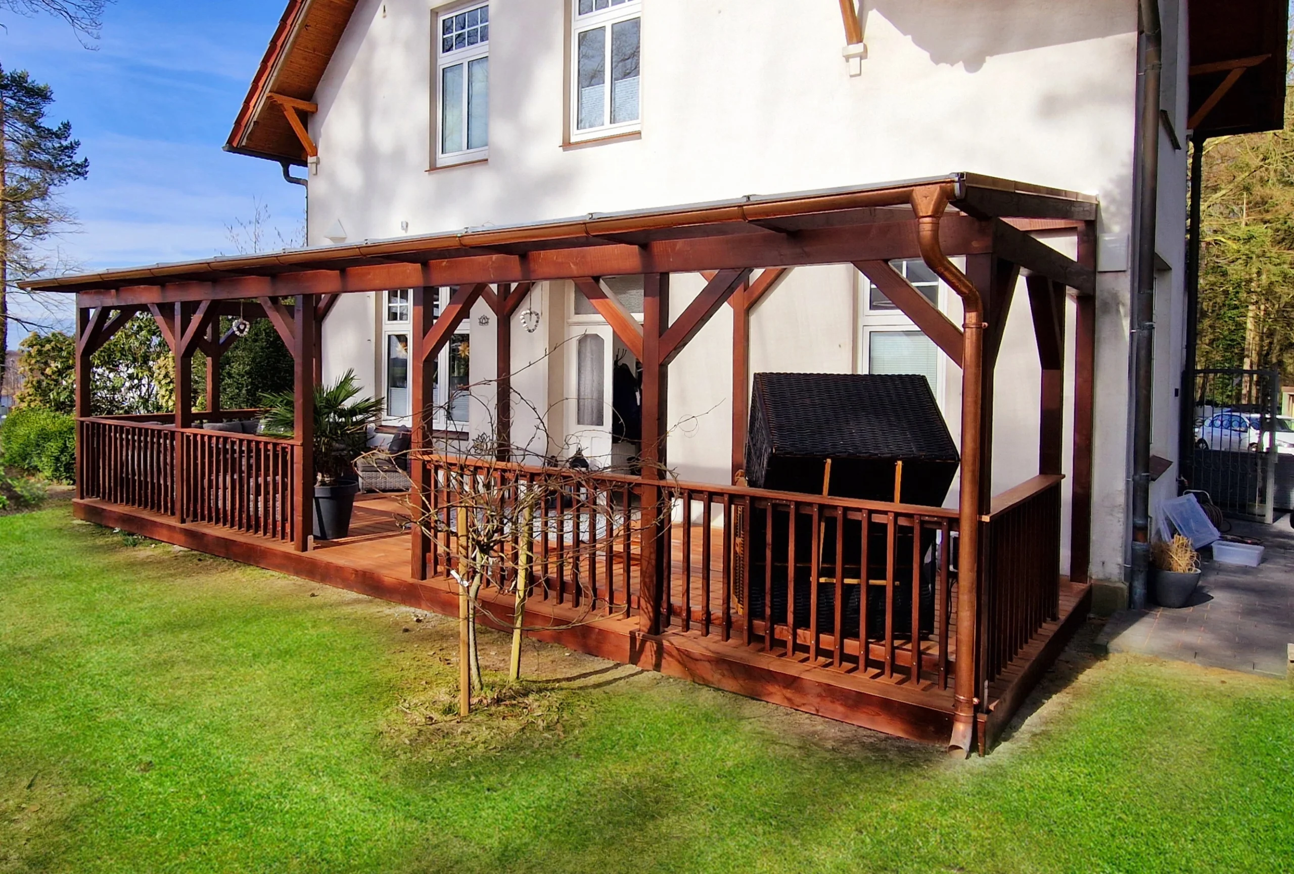 Eine elegante Holzterrasse mit Überdachung und Geländer, fachmännisch erstellt von Zimmerei Pawlowski GmbH, vor einem modernen Wohnhaus mit Garten.
