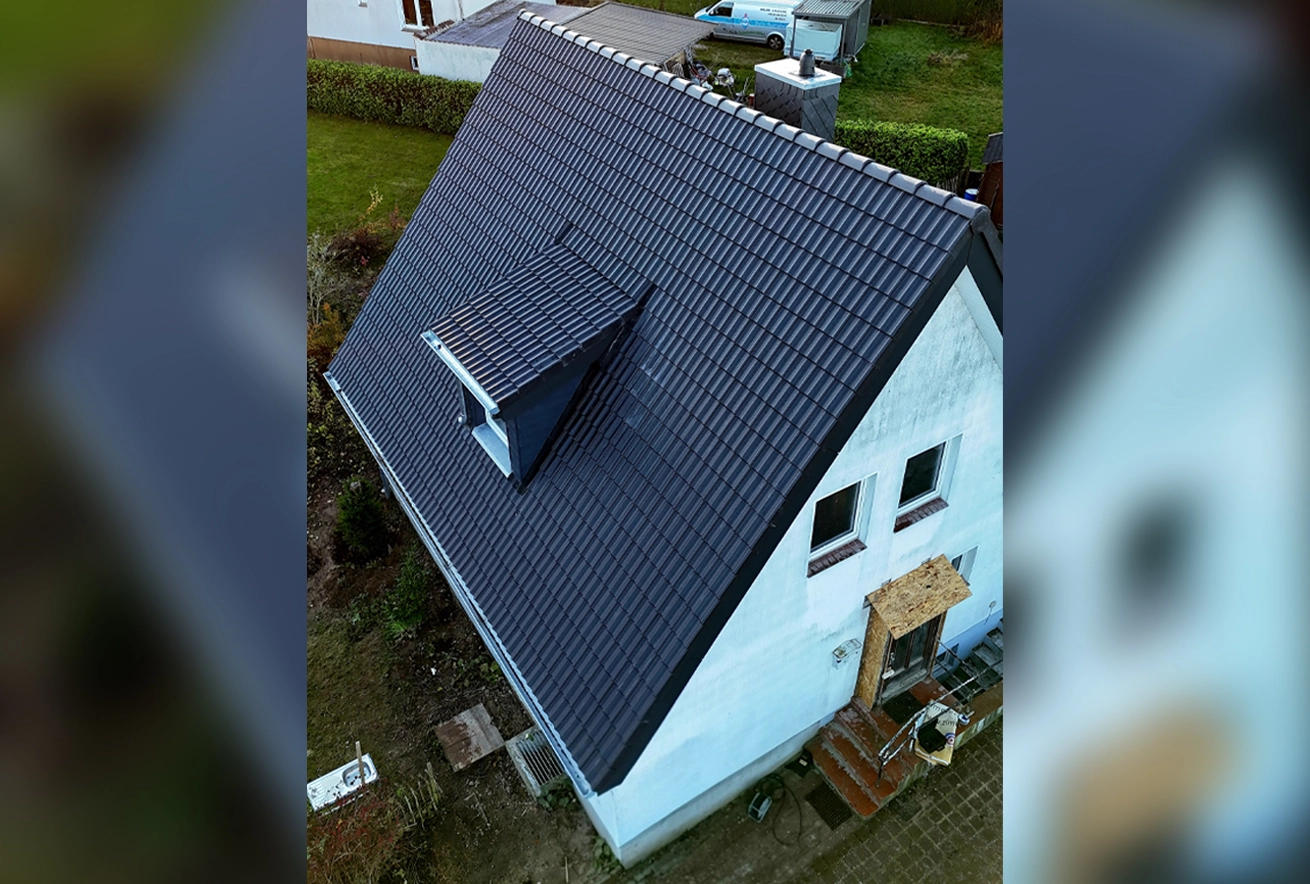 Luftaufnahme eines Einfamilienhauses mit neu gedecktem, dunkelgrauem Dach und moderner Dachgaube, ausgeführt von Zimmerei Pawlowski GmbH.