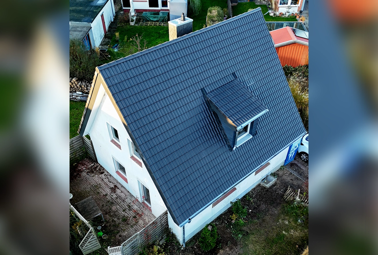 Luftaufnahme eines Einfamilienhauses mit neu gedecktem, dunkelgrauem Steildach und einer modernen Gaube, ein Referenzprojekt für hochwertige Dacharbeiten.
