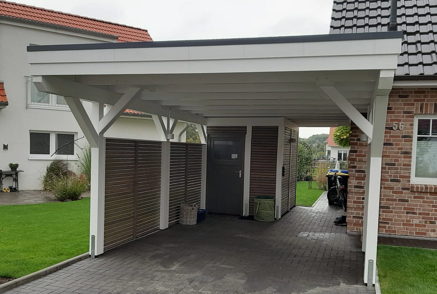 Modernes Holzcarport in Weiß mit integriertem Geräteschuppen aus Holzlamellen und seitlicher Sichtschutzwand, gefertigt von Zimmerei Pawlowski GmbH.