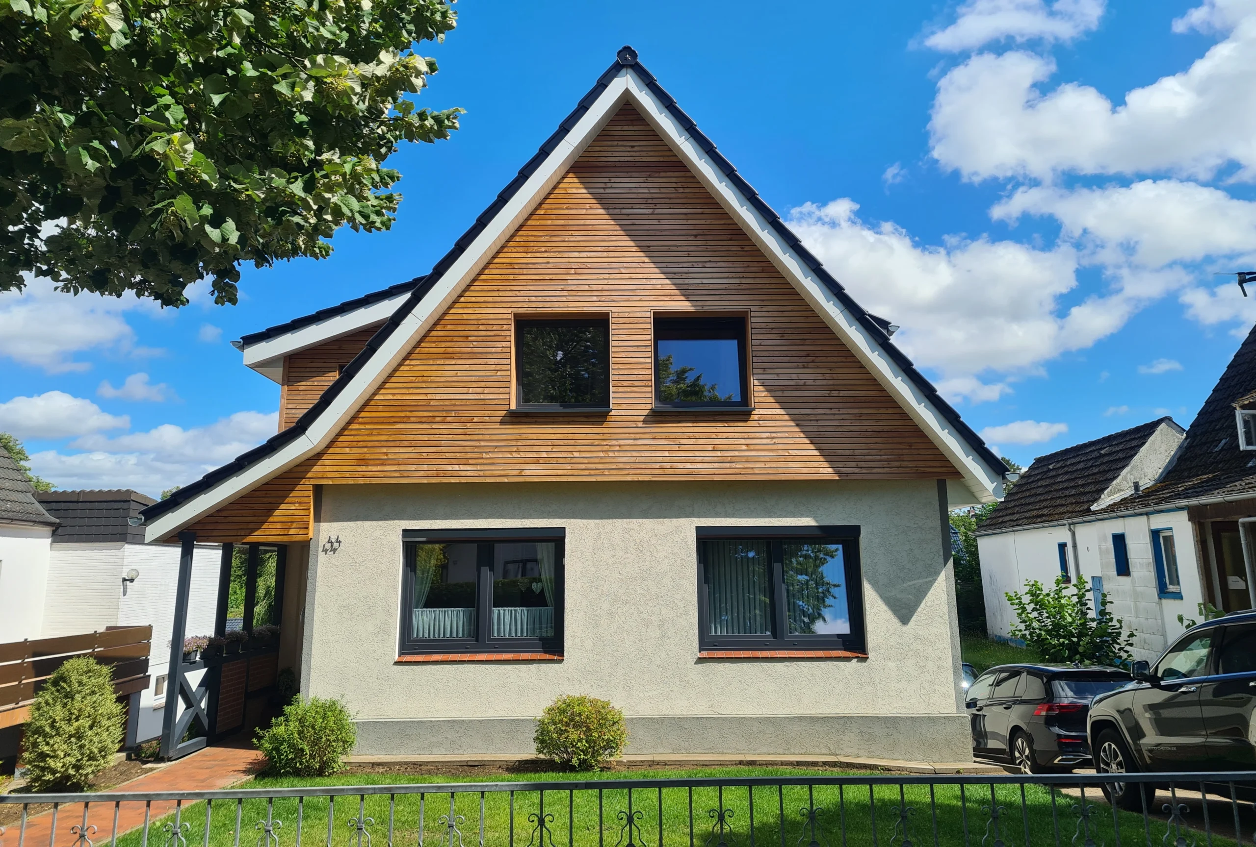 Modernes Einfamilienhaus mit eleganter Holzfassade im Giebelbereich und klassischem Satteldach, ein Beispiel für hochwertige Zimmereiarbeiten.