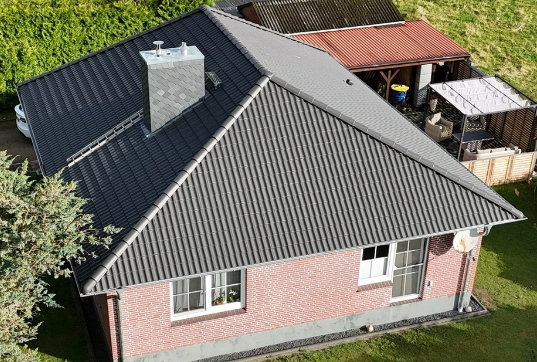 Referenzprojekt: Professionell gedecktes Dach eines Einfamilienhauses mit modernen anthrazitfarbenen Dachziegeln und passender Schornsteinverkleidung.