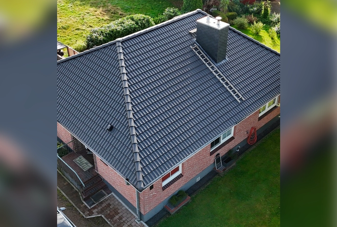 Draufsicht auf ein Einfamilienhaus mit neu gedecktem, dunkelgrauem Ziegeldach und Schornstein, bereit für die Abnahme nach der Dachsanierung.