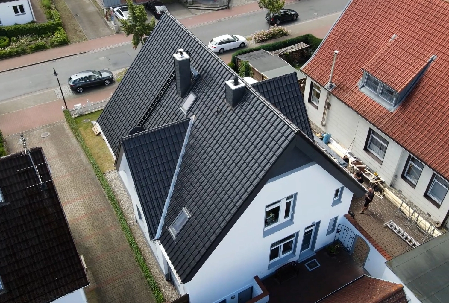 Luftaufnahme eines modernen Hauses mit neuem, dunkelgrauem Ziegeldach, Dachfenstern und Schornsteinen, das die Qualität der Dacheindeckung zeigt.