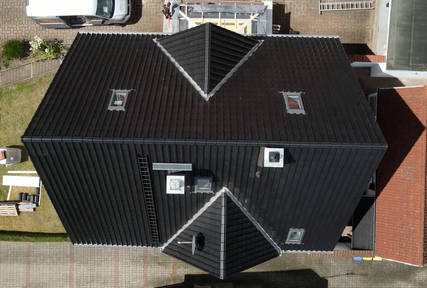 Draufsicht auf ein frisch gedecktes, dunkles Ziegeldach mit mehreren Dachfenstern und Installationen, ein Referenzprojekt der Zimmerei.