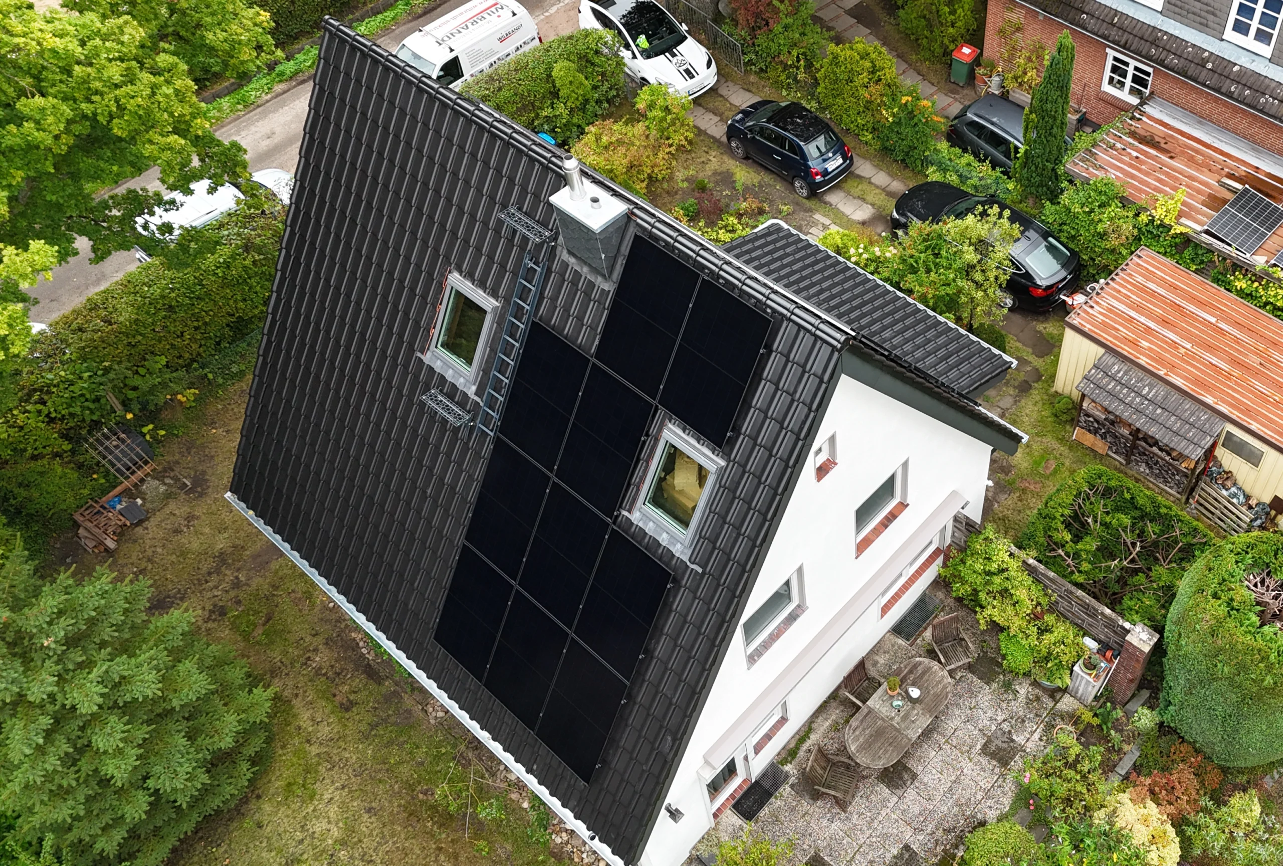 Luftaufnahme eines sanierten Daches mit dunklen Ziegeln, integrierter Solaranlage und neuen Dachfenstern, ein Beispiel für hochwertige Zimmereiarbeiten.