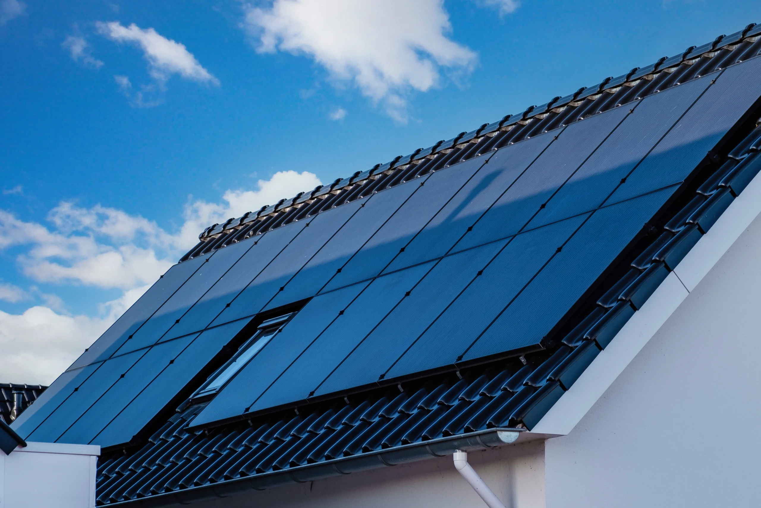 Dach eines modernen Hauses mit Photovoltaikanlage und Dachfenster, symbolisiert nachhaltige Energie und professionelle Dacharbeiten.