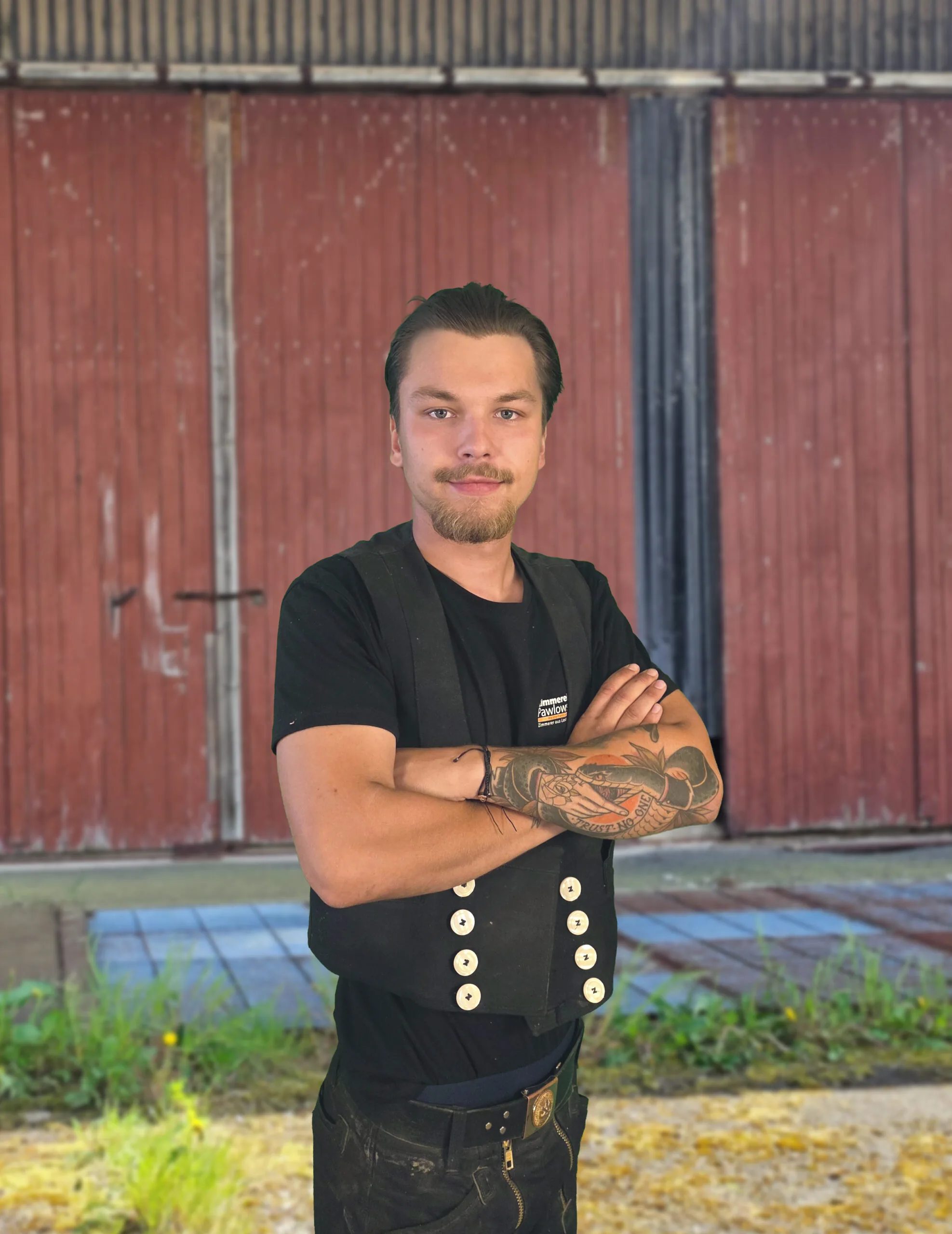 Ein Zimmermann des Teams der Zimmerei Pawlowski in traditioneller Arbeitskleidung vor einem Holztor.